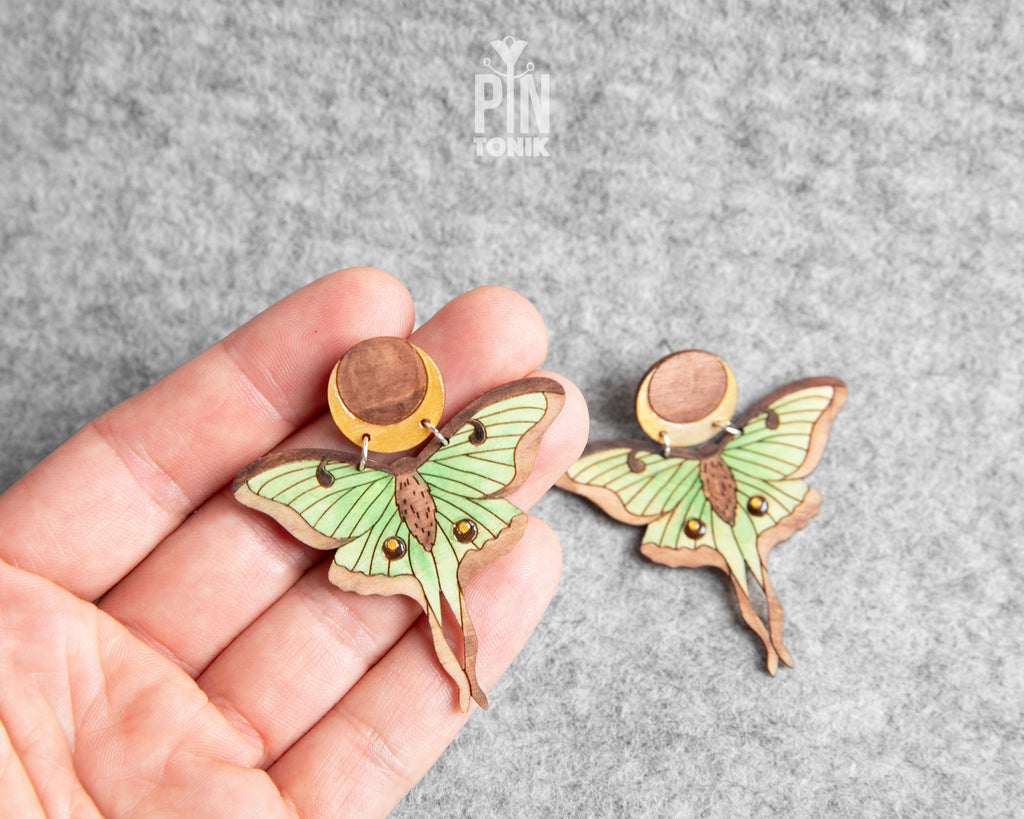 Hand-painted wooden Luna Moth stud earrings featuring green wings and a natural wood-grain moon detail with stainless steel posts