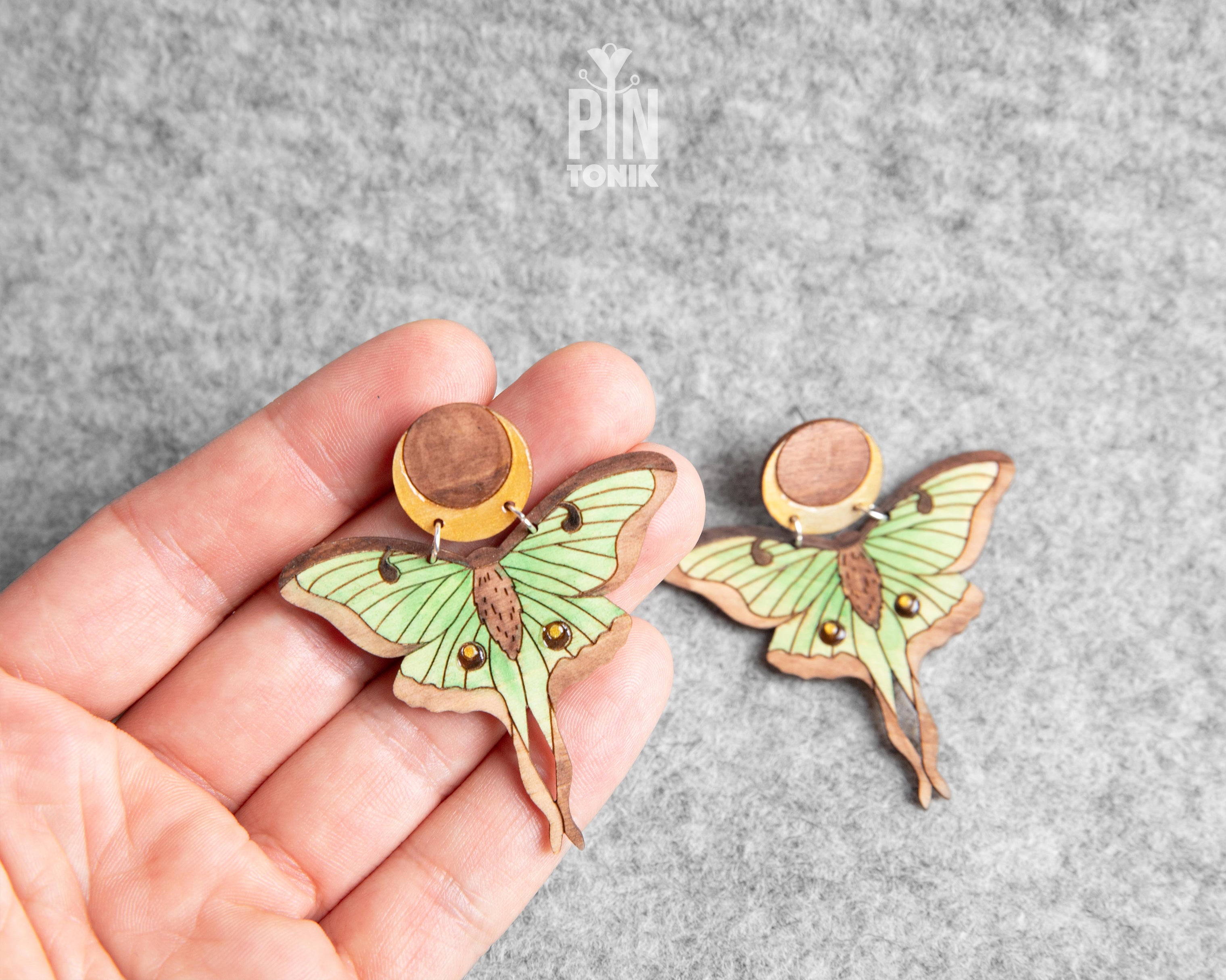 Hand-painted wooden Luna Moth stud earrings featuring green wings and a natural wood-grain moon detail with stainless steel posts