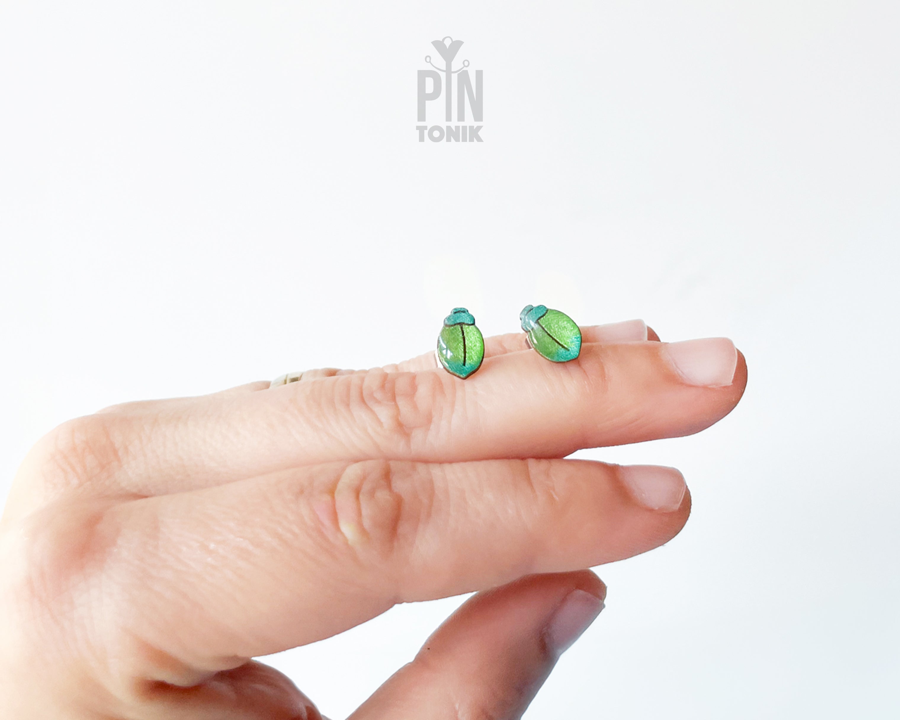 Handmade wooden milkweed beetle stud earrings with a shimmering iridescent green and blue finish by PinTonik.