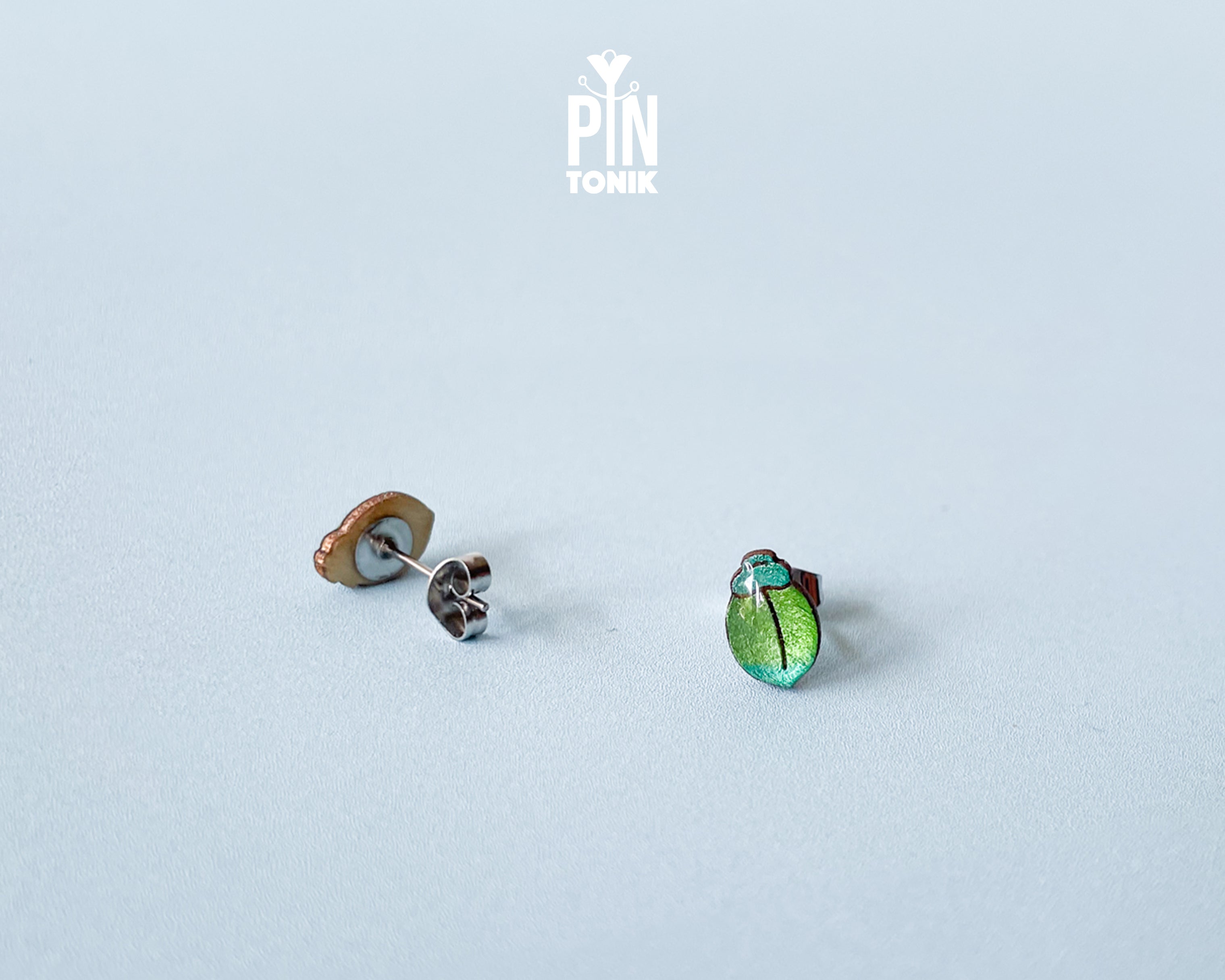 Handmade wooden milkweed beetle stud earrings with a shimmering iridescent green and blue finish by PinTonik.