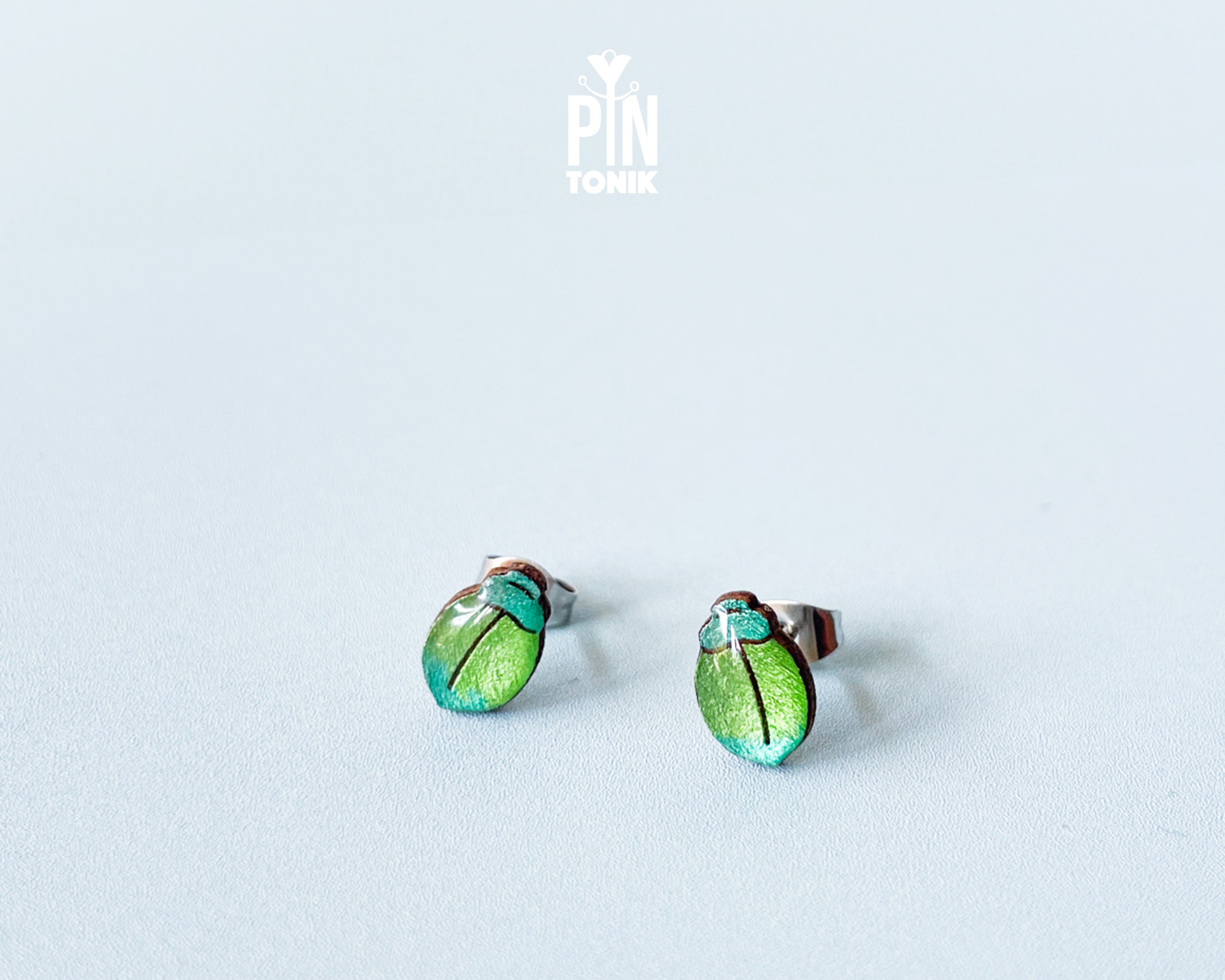 Handmade wooden milkweed beetle stud earrings with a shimmering iridescent green and blue finish by PinTonik.
