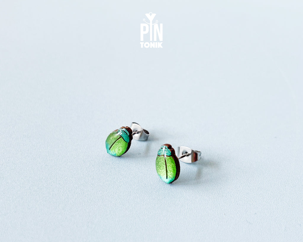 Handmade wooden milkweed beetle stud earrings with a shimmering iridescent green and blue finish by PinTonik.