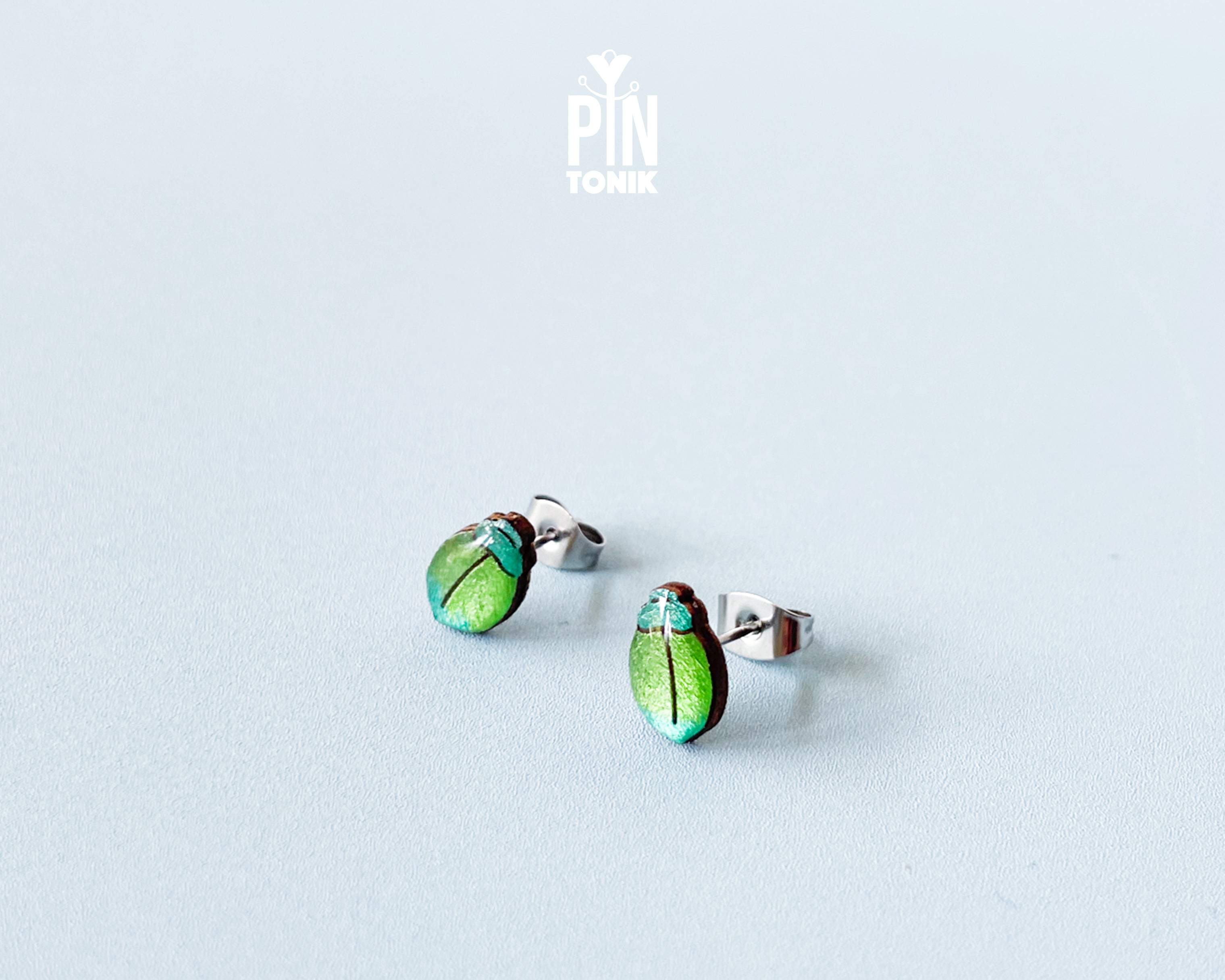 Handmade wooden milkweed beetle stud earrings with a shimmering iridescent green and blue finish by PinTonik.