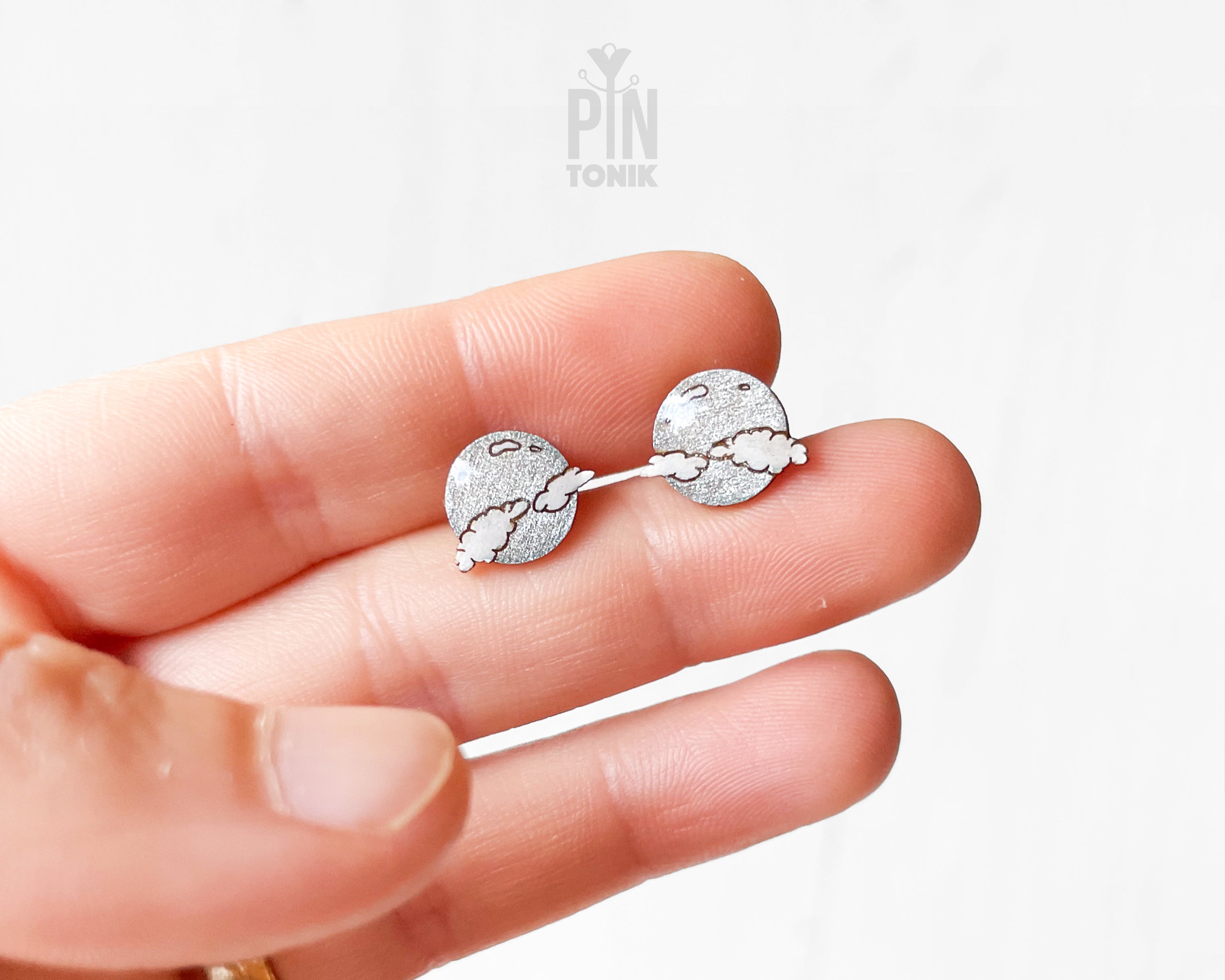 Handmade wooden celestial stud earrings featuring a silver glitter crescent moon behind a white cloud by PinTonik.