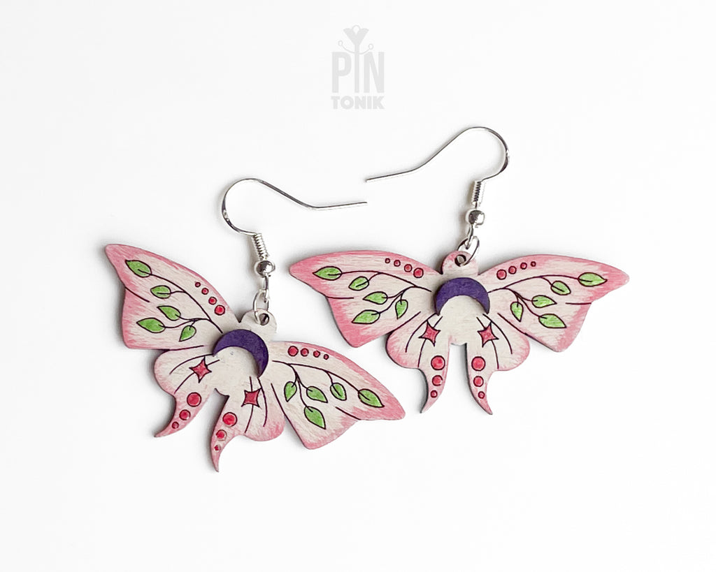 Hand-painted wooden Luna Moth dangle earrings featuring pink wings, green leaf patterns, and purple moon phases on sterling silver hooks