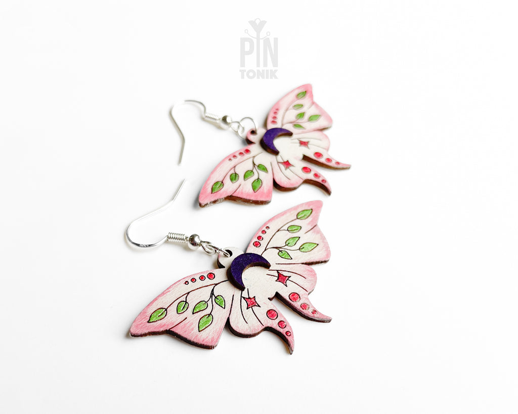 Hand-painted wooden Luna Moth dangle earrings featuring pink wings, green leaf patterns, and purple moon phases on sterling silver hooks