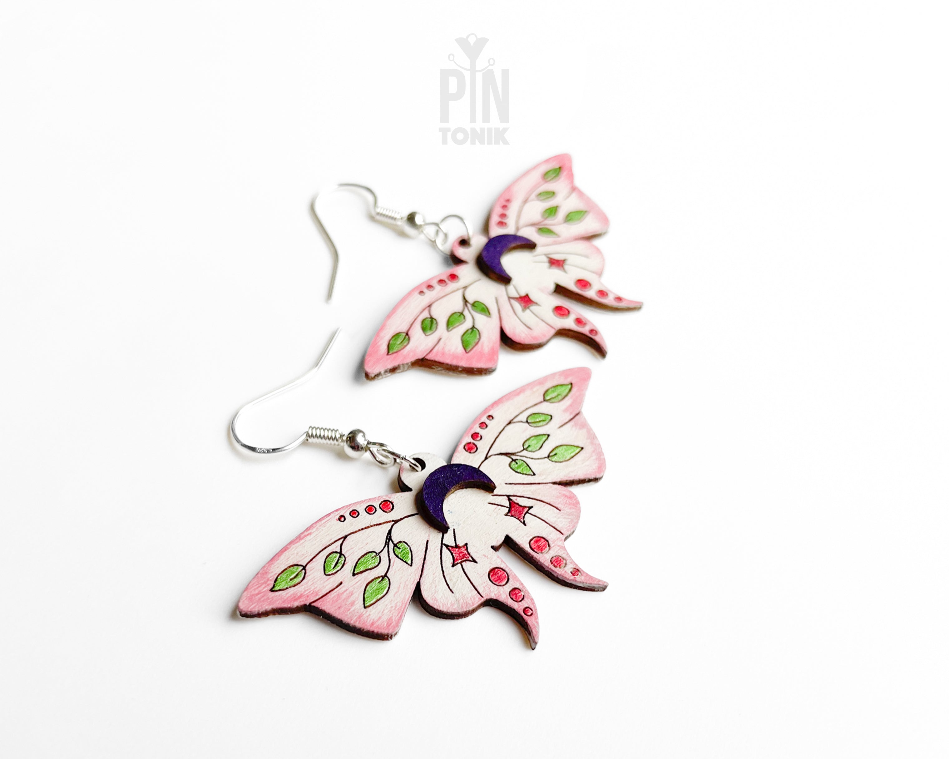 Hand-painted wooden Luna Moth dangle earrings featuring pink wings, green leaf patterns, and purple moon phases on sterling silver hooks