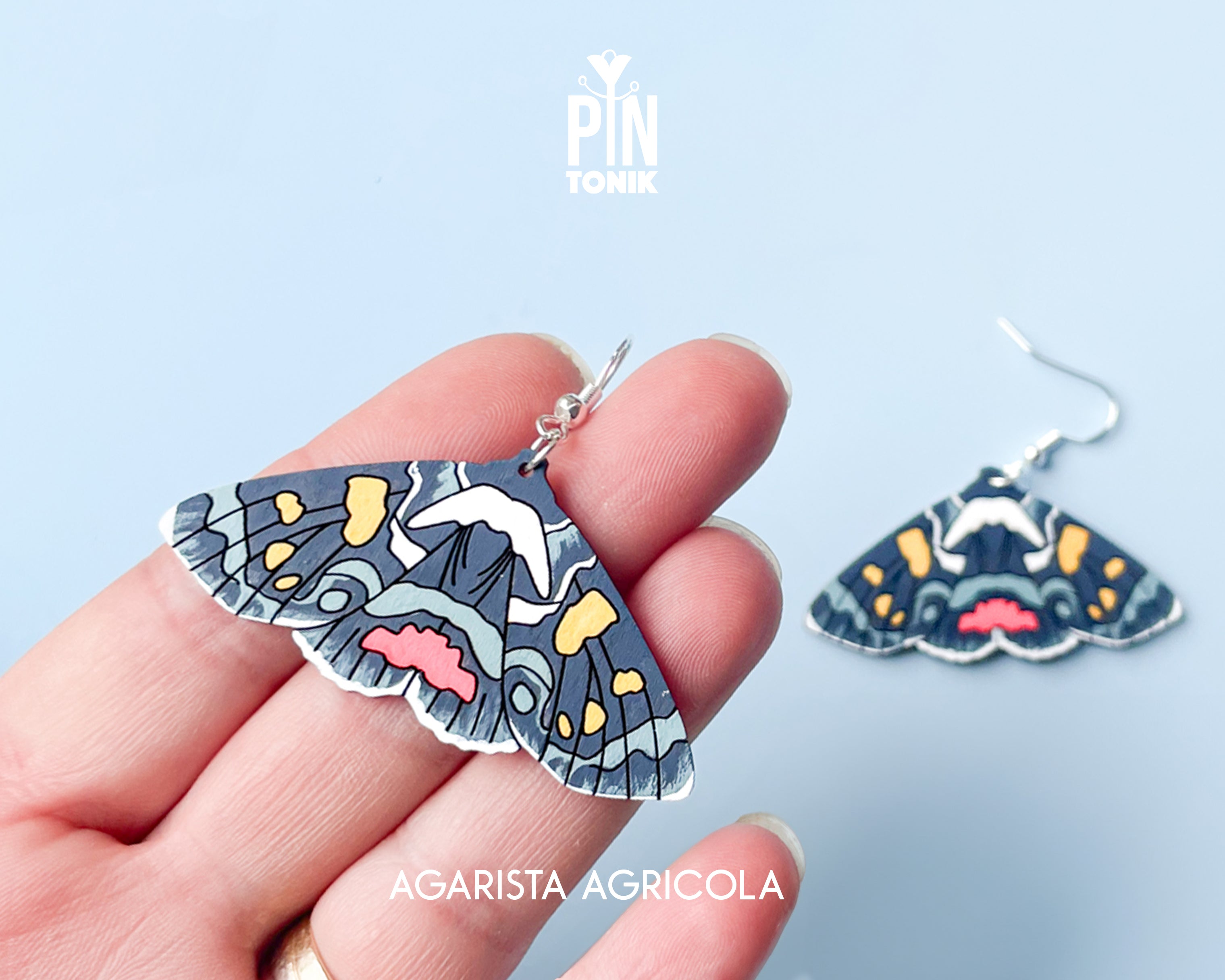 Large hand-painted wooden Agarista Agricola moth dangle earrings with intricate navy, pink, and yellow wing patterns on sterling silver hooks
