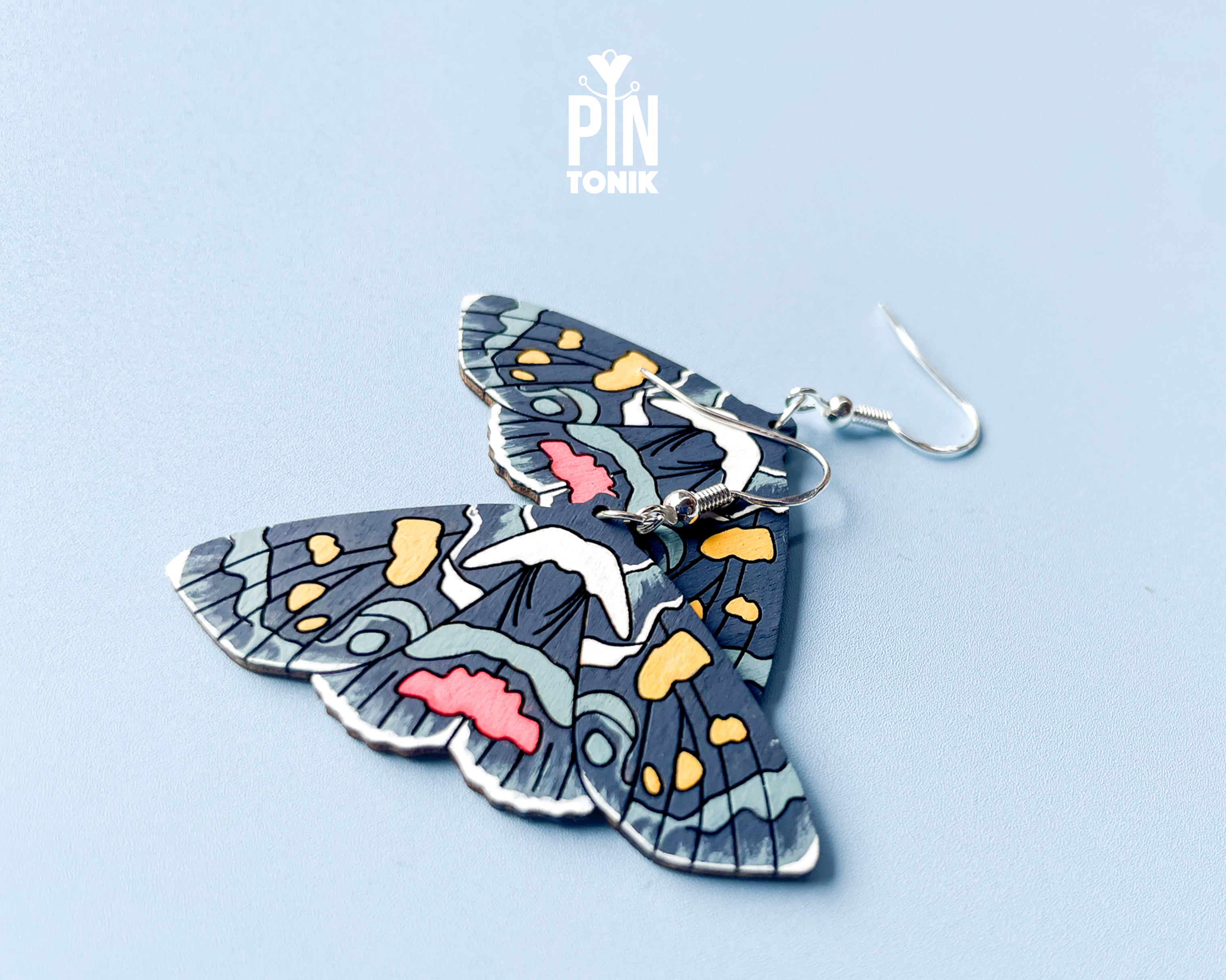Large hand-painted wooden Agarista Agricola moth dangle earrings with intricate navy, pink, and yellow wing patterns on sterling silver hooks