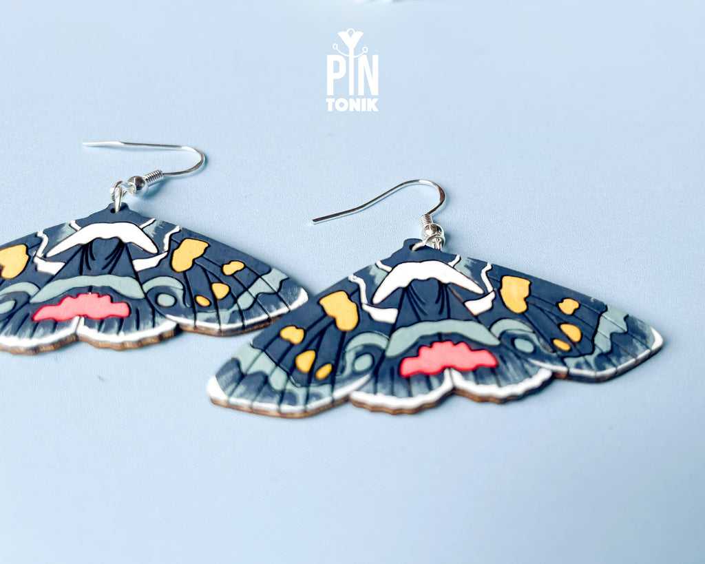 Large hand-painted wooden Agarista Agricola moth dangle earrings with intricate navy, pink, and yellow wing patterns on sterling silver hooks