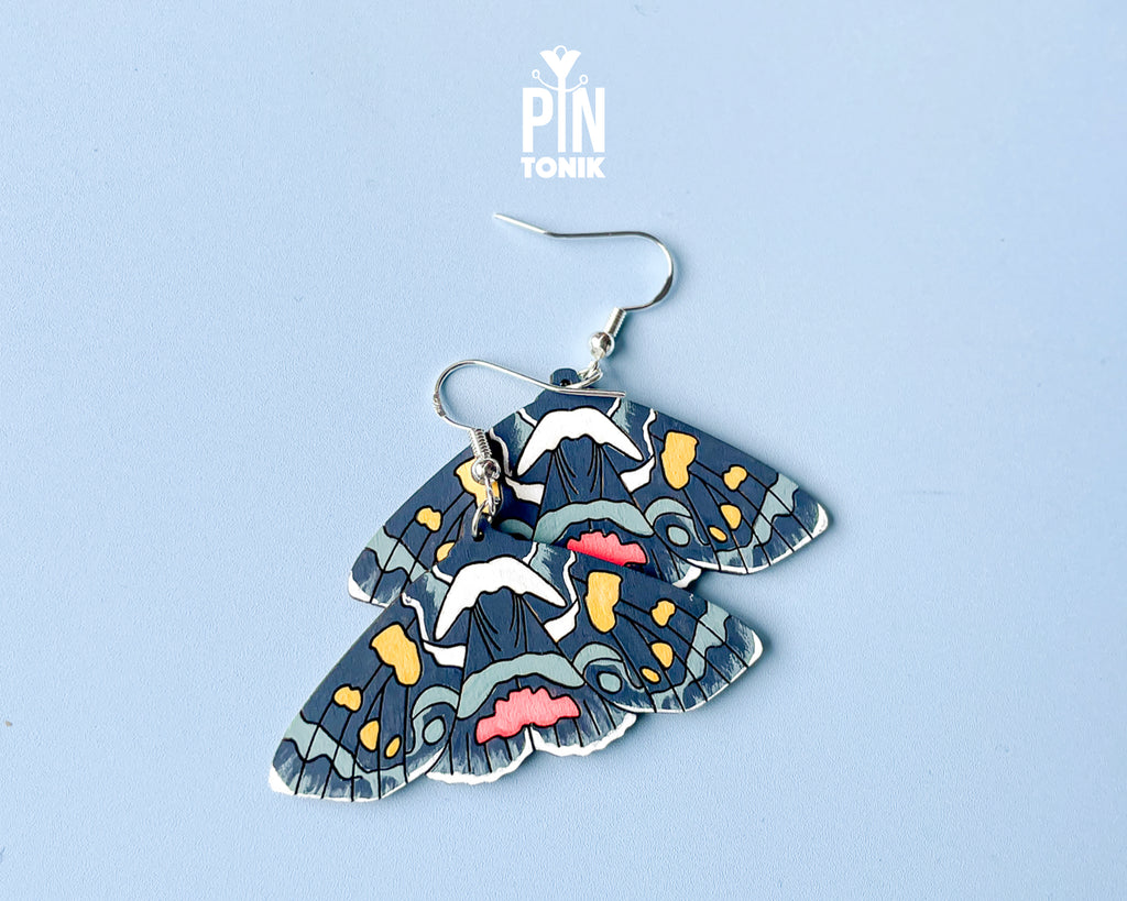 Large hand-painted wooden Agarista Agricola moth dangle earrings with intricate navy, pink, and yellow wing patterns on sterling silver hooks