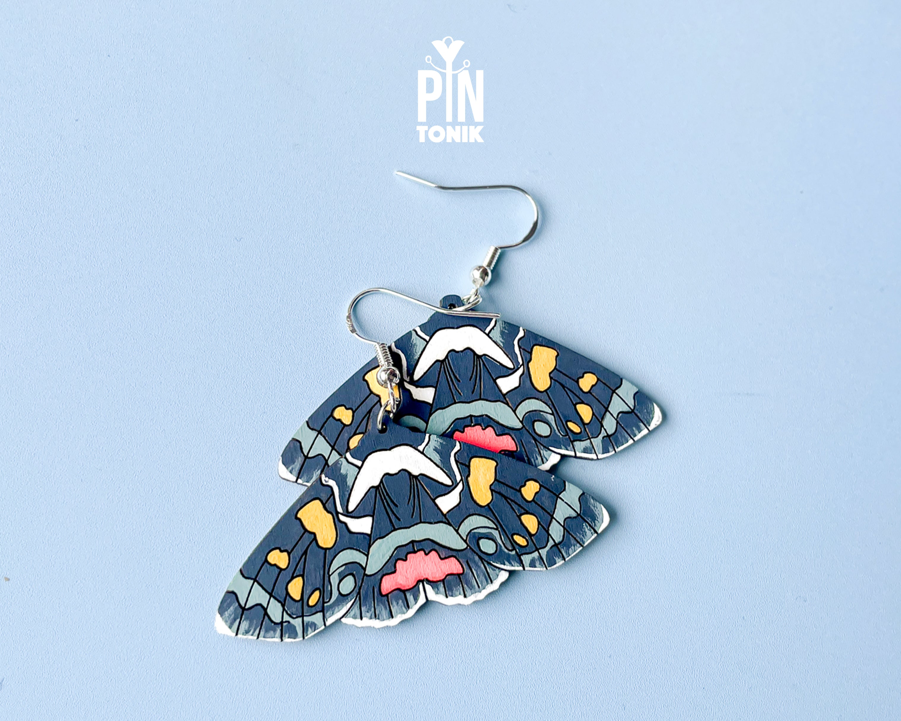 Large hand-painted wooden Agarista Agricola moth dangle earrings with intricate navy, pink, and yellow wing patterns on sterling silver hooks