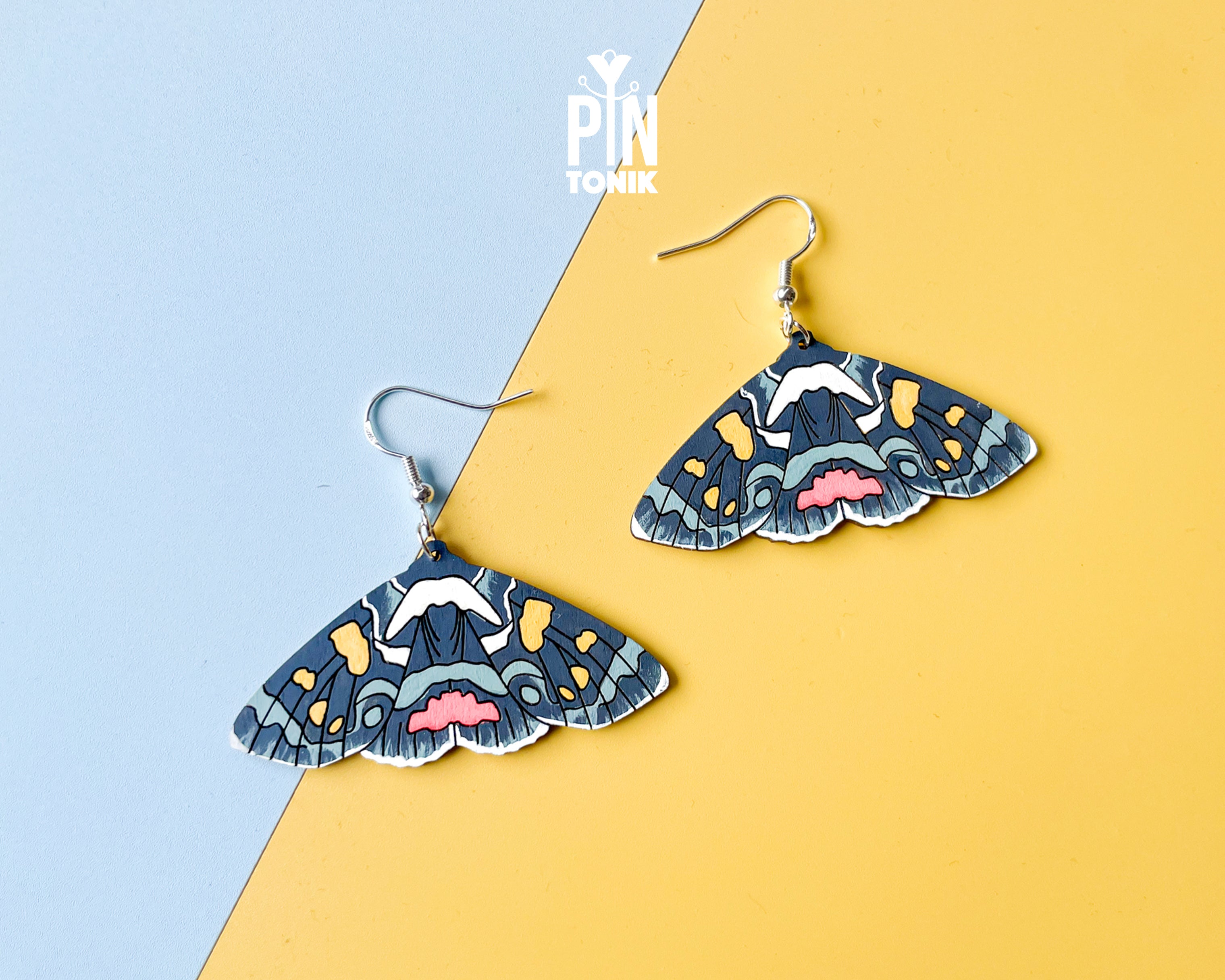 Large hand-painted wooden Agarista Agricola moth dangle earrings with intricate navy, pink, and yellow wing patterns on sterling silver hooks