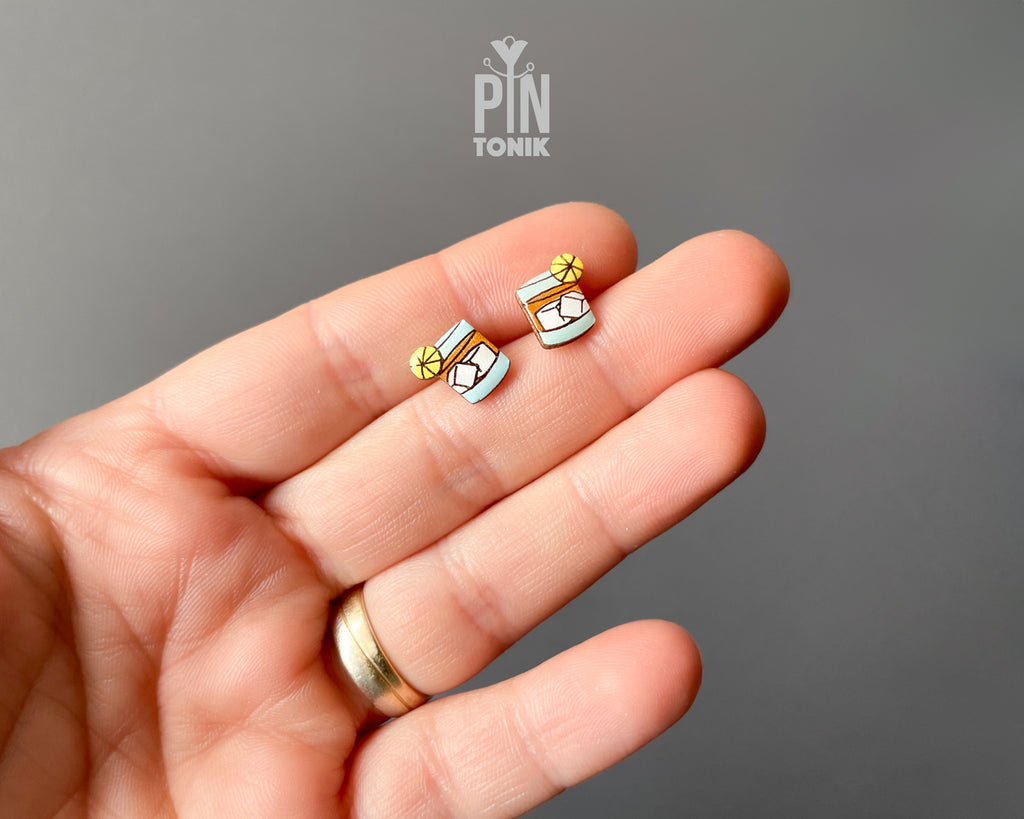 Handmade wooden cocktail tumbler stud earrings with a blue drink, ice cubes, and an orange wheel garnish by PinTonik.
