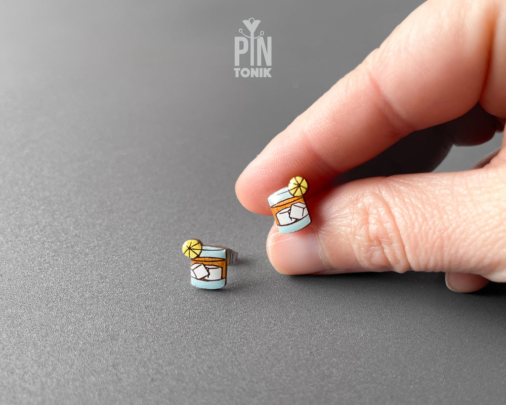 Handmade wooden cocktail tumbler stud earrings with a blue drink, ice cubes, and an orange wheel garnish by PinTonik.