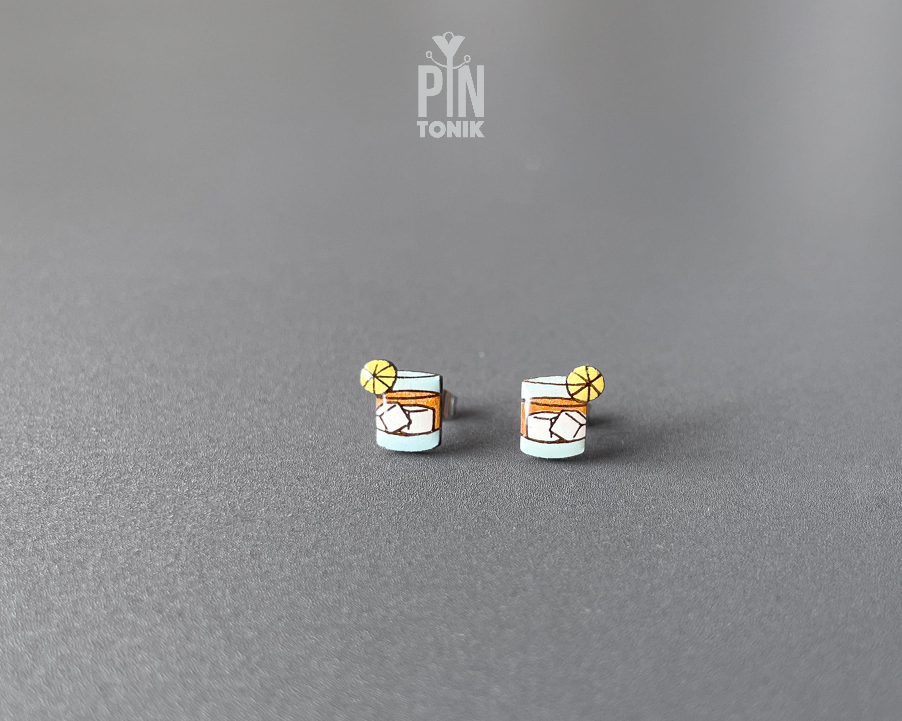 Handmade wooden cocktail tumbler stud earrings with a blue drink, ice cubes, and an orange wheel garnish by PinTonik.
