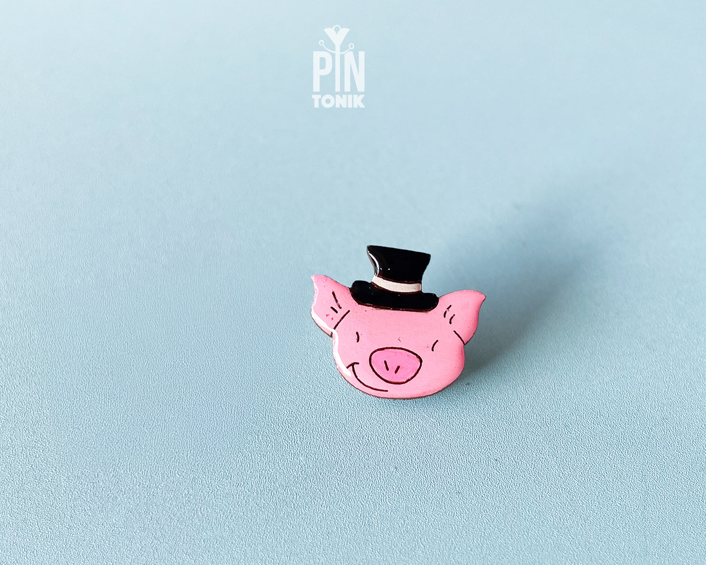Hand-painted pink wooden pig pin wearing a black top hat with a high-gloss resin finish