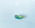 Hand-painted wooden pickle pin with light and dark green gradients and detailed textures, shown on a light blue background.