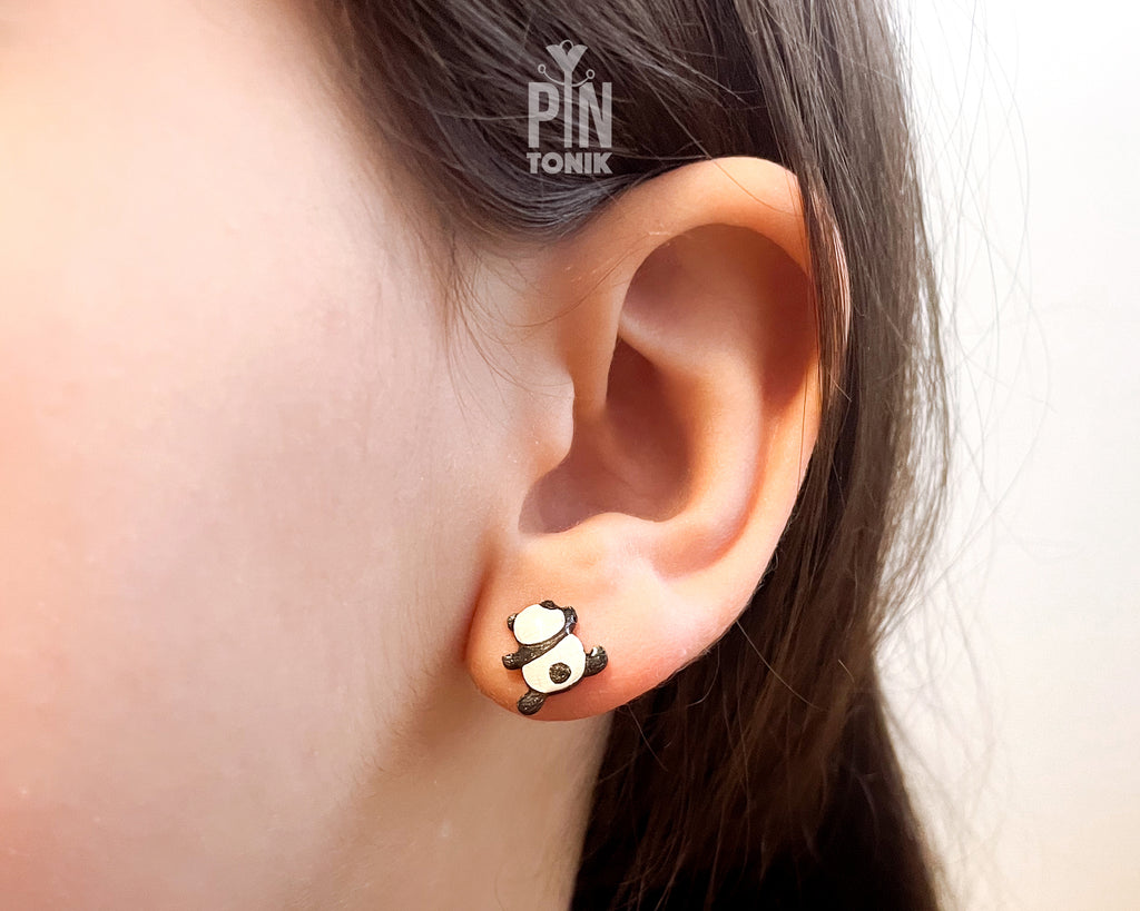 Pair of hand-painted wooden climbing panda stud earrings that appear to be hanging from the earlobe, finished with glossy resin