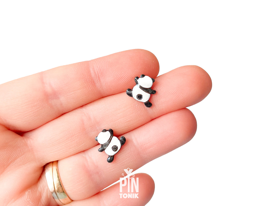 Pair of hand-painted wooden climbing panda stud earrings that appear to be hanging from the earlobe, finished with glossy resin