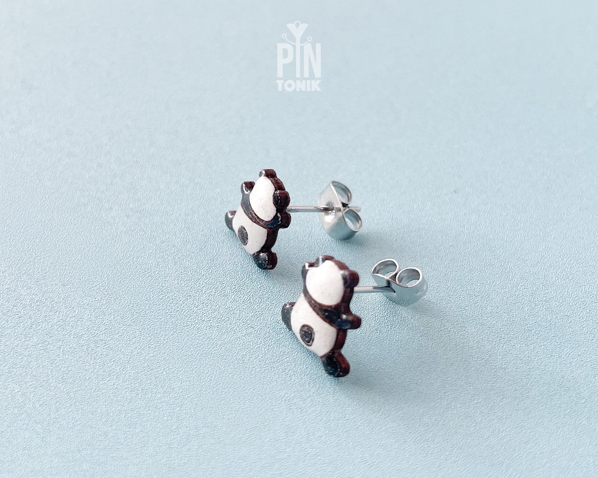 Pair of hand-painted wooden climbing panda stud earrings that appear to be hanging from the earlobe, finished with glossy resin