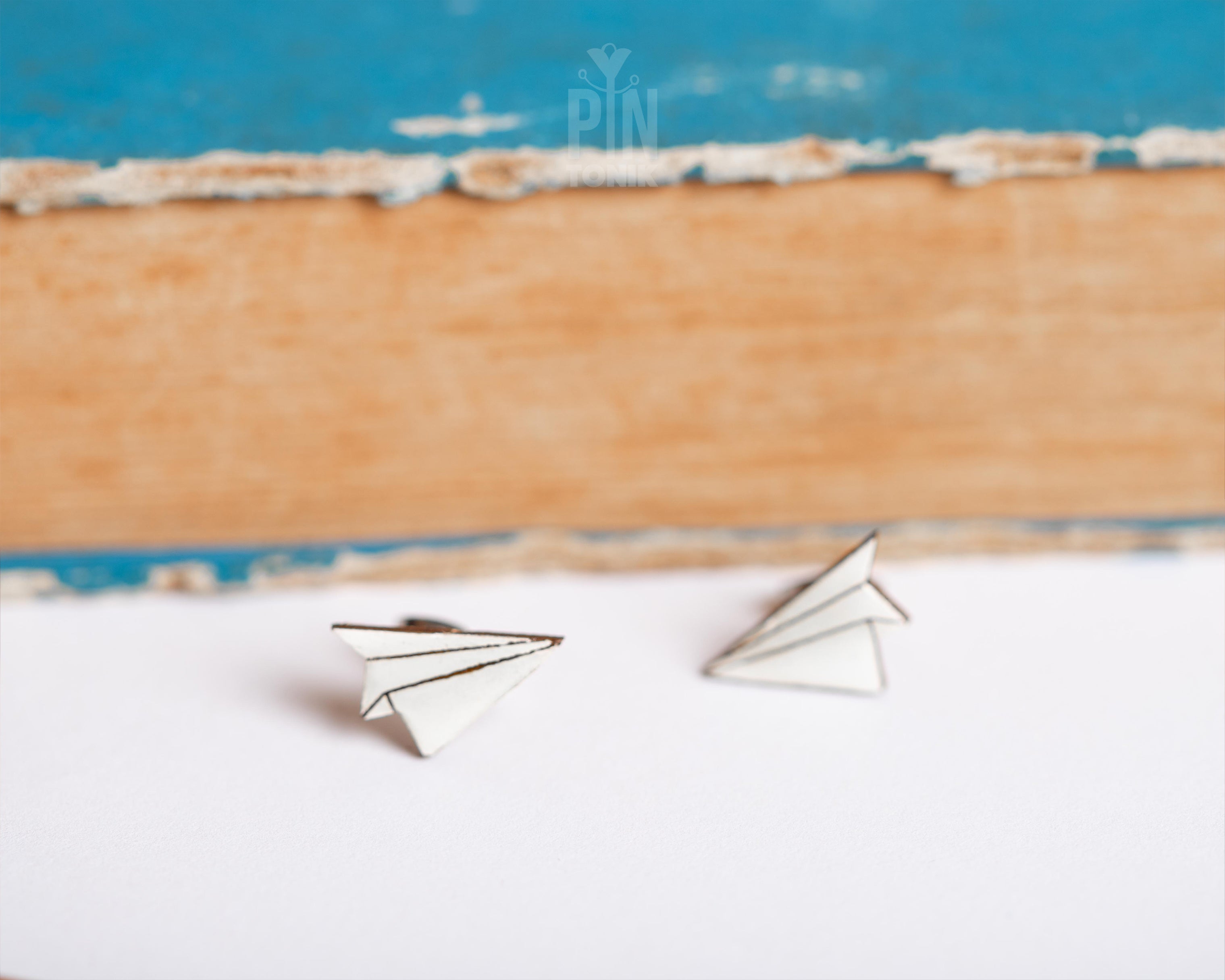 A pair of small white paper airplane stud earrings resting on a white surface