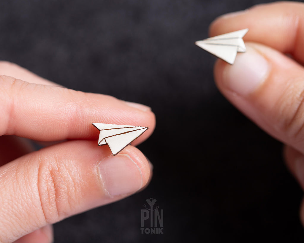 Handmade wooden paper airplane stud earrings in bright white with fine black hand-drawn crease lines by PinTonik.