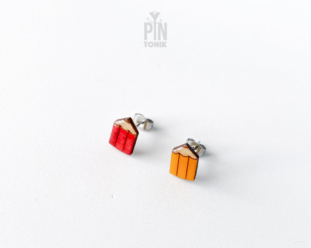 A pair of small stud earrings shaped like pencils, one red and one yellow, with Stainless steel posts, shown on a plain white background with a PIN TONIK watermark at the top.