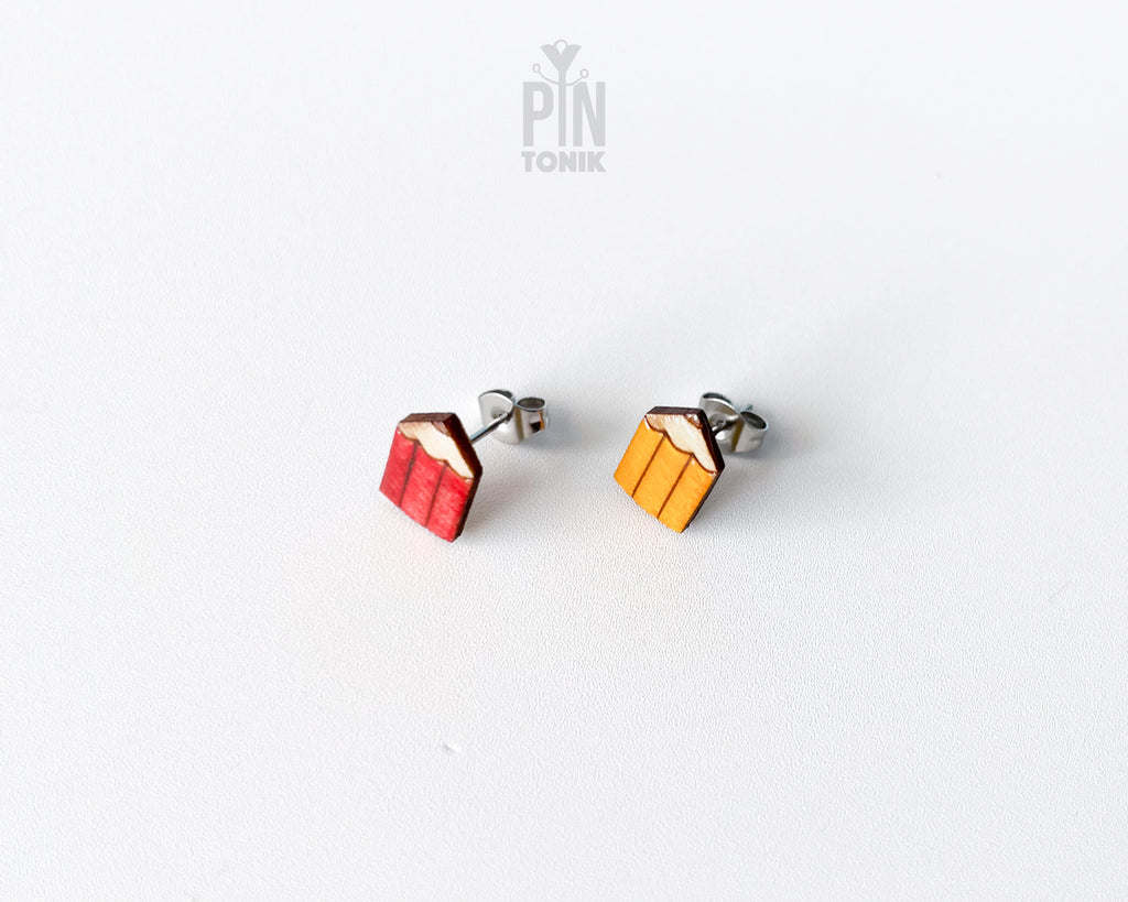 Handmade wooden mismatched stud earrings featuring a sharpened red colored pencil on one ear and yellow pencil on the other by PinTonik.