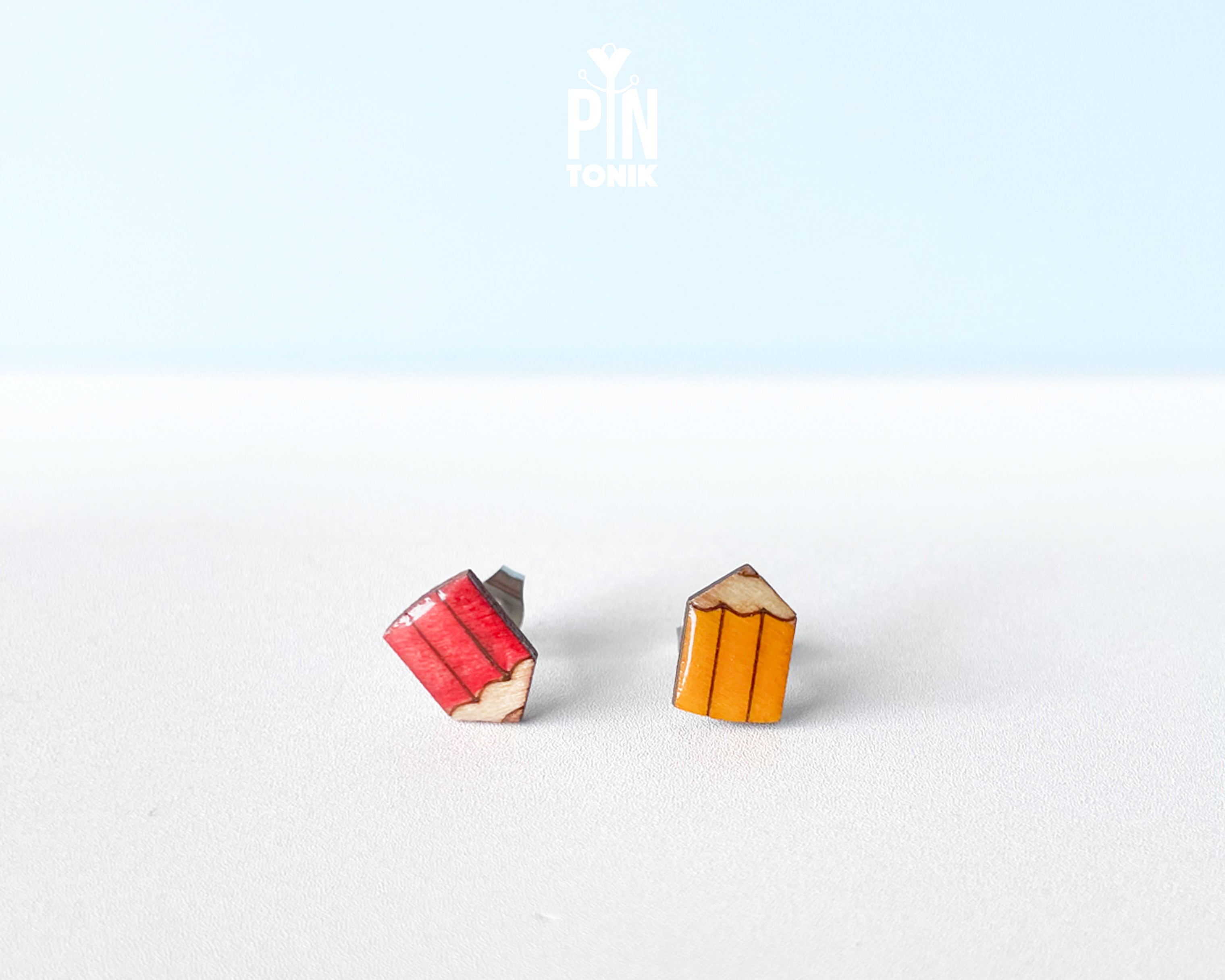 Handmade wooden mismatched stud earrings featuring a sharpened red colored pencil on one ear and yellow pencil on the other by PinTonik.
