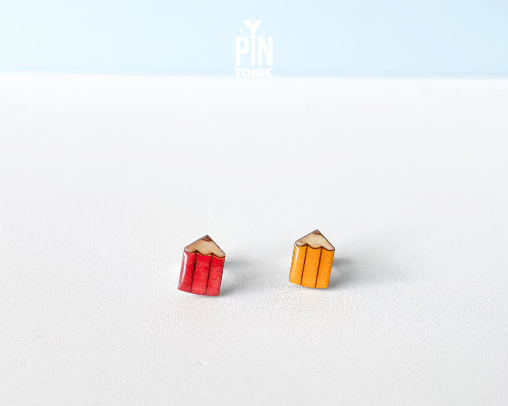 Handmade wooden mismatched stud earrings featuring a sharpened red colored pencil on one ear and yellow pencil on the other by PinTonik.