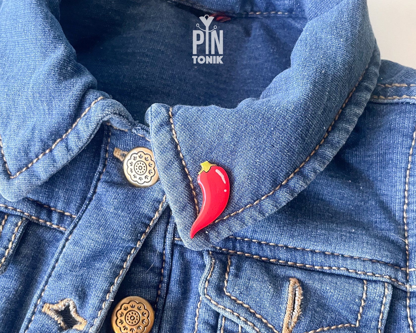 Hand-painted wooden red chili pepper pin with a glossy finish and a yellow stem, shown next to its stainless steel clutch back on a light blue-grey background