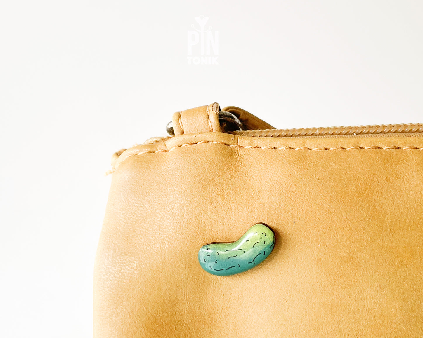 Hand-painted wooden pickle pin with light and dark green gradients and detailed textures, shown on a light blue background.