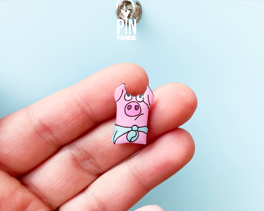 Hand-painted pink wooden pig pin wearing a blue bandana with a high-gloss resin finish