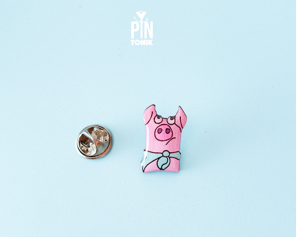 Hand-painted pink wooden pig pin wearing a blue bandana with a high-gloss resin finish
