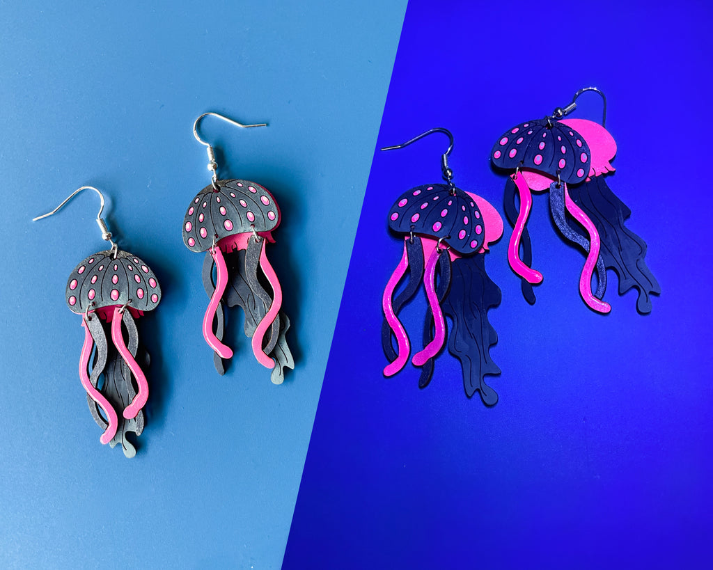 Hand-painted wooden jellyfish dangle earrings with charcoal grey bodies and vibrant neon pink tentacles on sterling silver hooks
