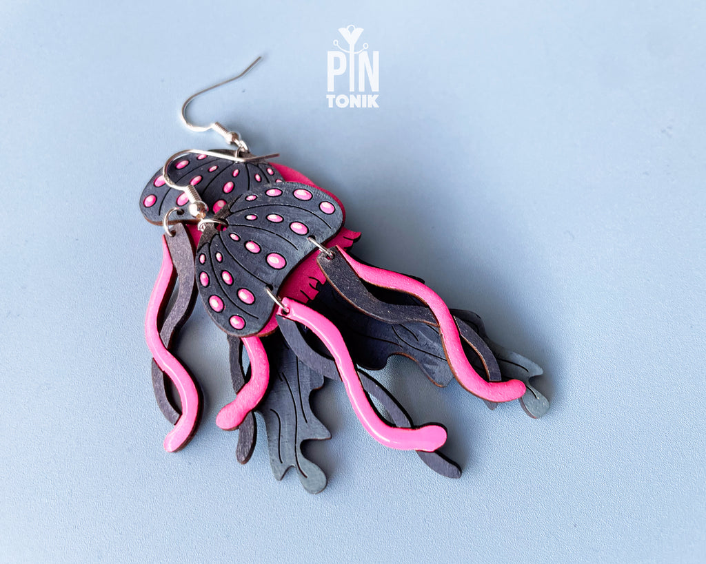 Hand-painted wooden jellyfish dangle earrings with charcoal grey bodies and vibrant neon pink tentacles on sterling silver hooks
