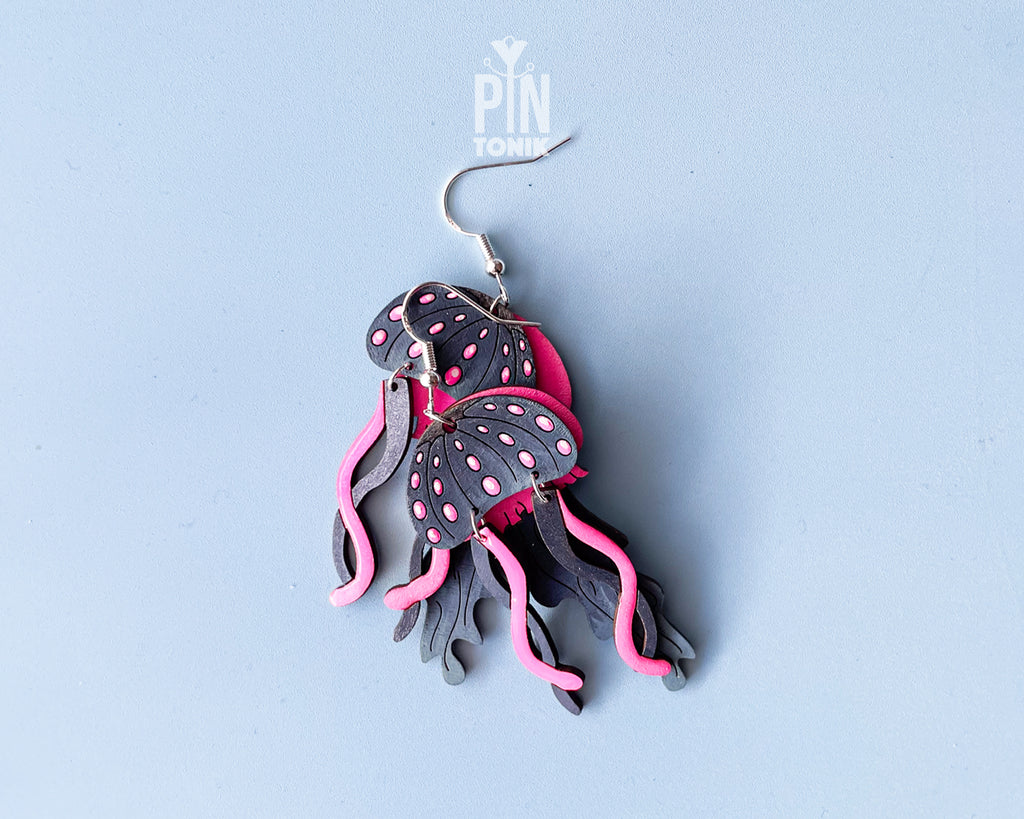 Hand-painted wooden jellyfish dangle earrings with charcoal grey bodies and vibrant neon pink tentacles on sterling silver hooks