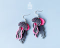 Hand-painted wooden jellyfish dangle earrings with charcoal grey bodies and vibrant neon pink tentacles on sterling silver hooks