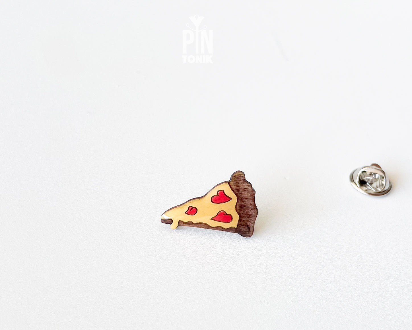 Hand-painted wooden pizza slice pin with heart-shaped pepperonis and a glossy finish, shown next to a stainless steel clutch back on a white background.
