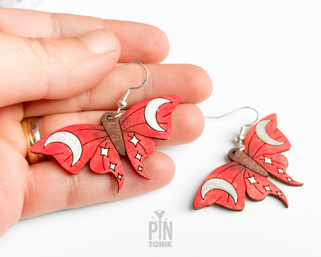Hand-painted red wooden moth dangle earrings with silver crescent moon and white star details on sterling silver hooks