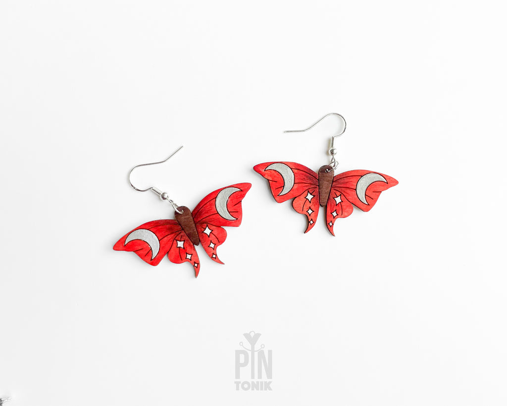 Hand-painted red wooden moth dangle earrings with silver crescent moon and white star details on sterling silver hooks
