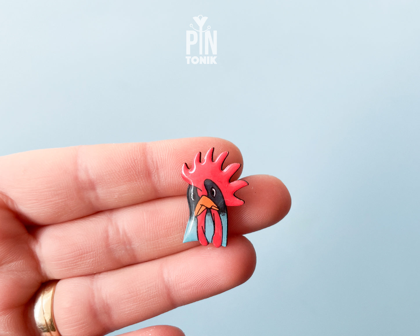 Hand-painted wooden rooster pin with a vibrant red comb and blue neck detail, finished with high-gloss resin