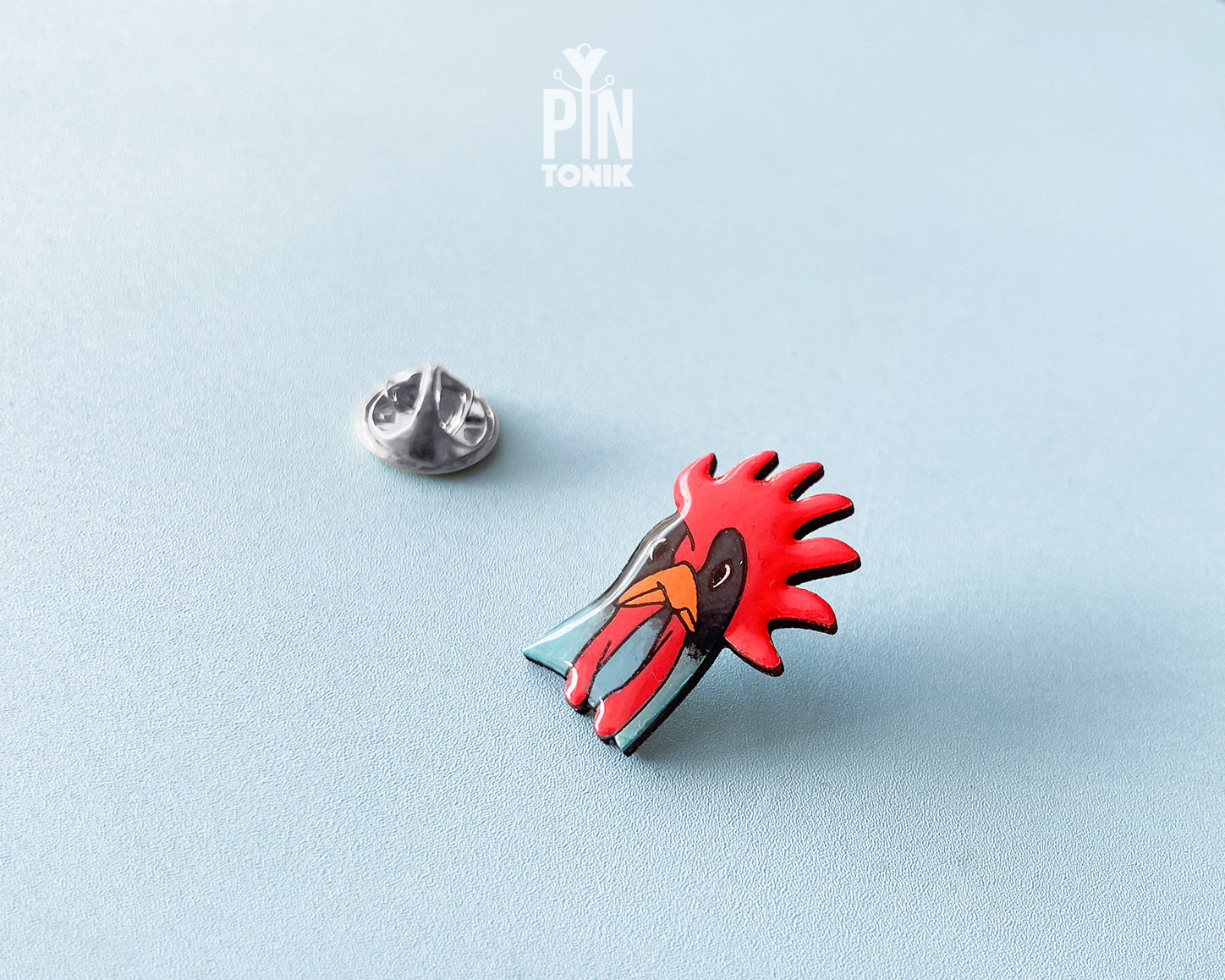 Hand-painted wooden rooster pin with a vibrant red comb and blue neck detail, finished with high-gloss resin