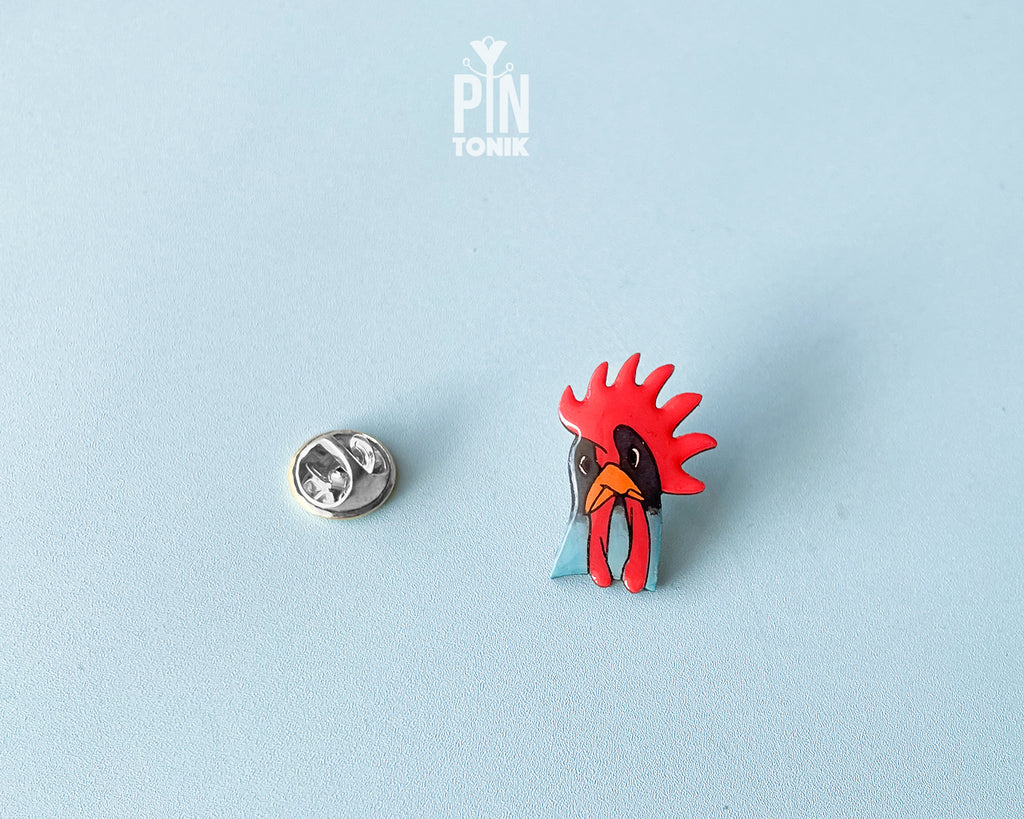 Hand-painted wooden rooster pin with a vibrant red comb and blue neck detail, finished with high-gloss resin