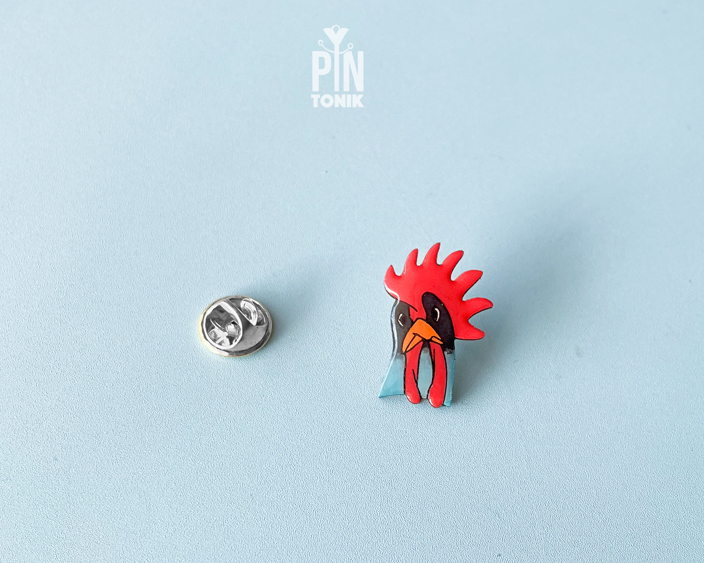 Hand-painted wooden rooster pin with a vibrant red comb and blue neck detail, finished with high-gloss resin