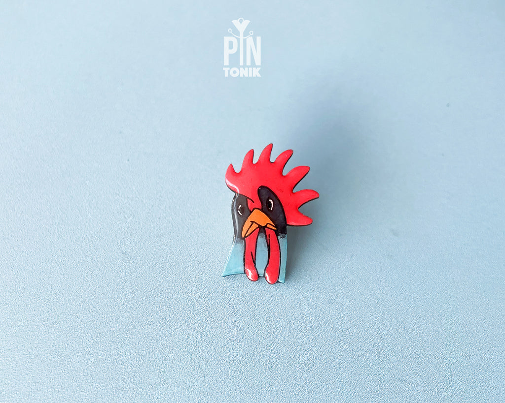 Hand-painted wooden rooster pin with a vibrant red comb and blue neck detail, finished with high-gloss resin