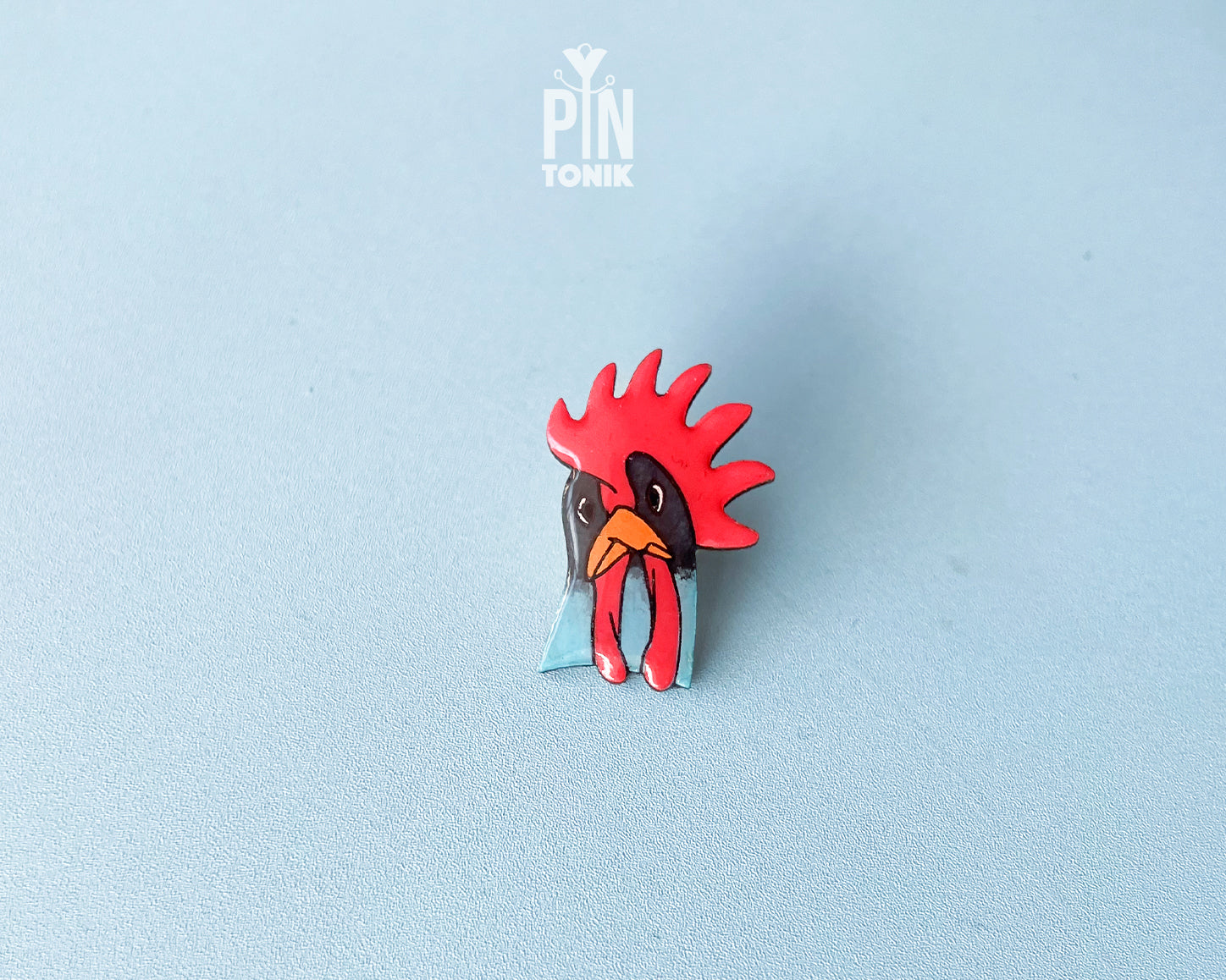 Hand-painted wooden rooster pin with a vibrant red comb and blue neck detail, finished with high-gloss resin