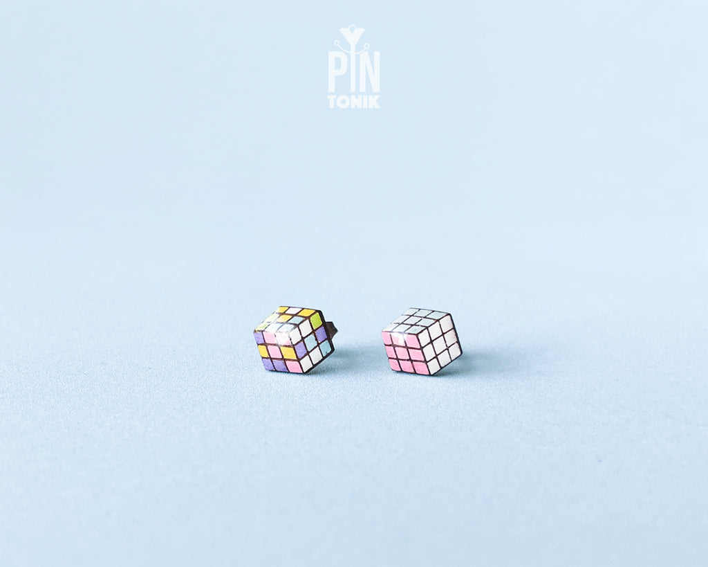 A pair of cube-shaped wooden stud earrings with colorful puzzle-cube faces, displayed on a light blue background with a 'PIN TONIK' logo at the top.