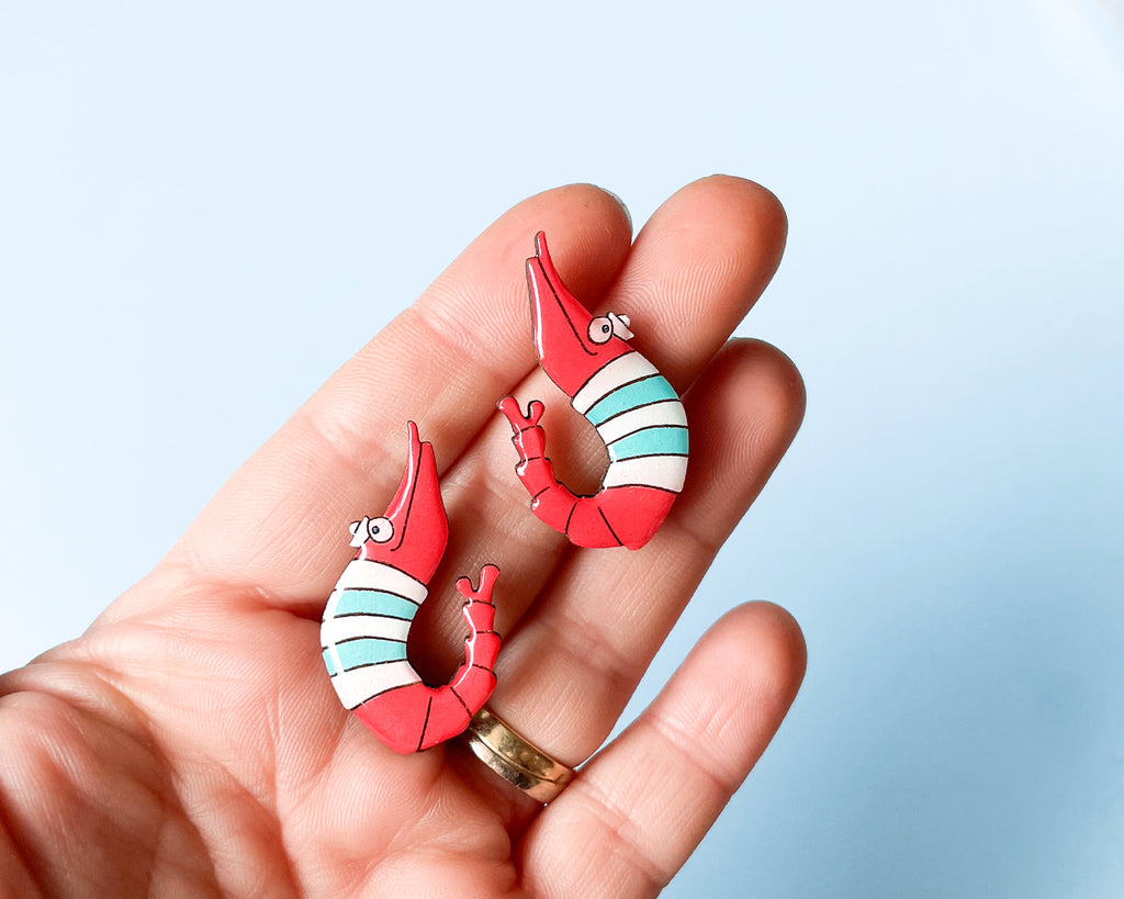 Pair of hand-painted wooden shrimp stud earrings with red and teal stripes and funny wide eyes